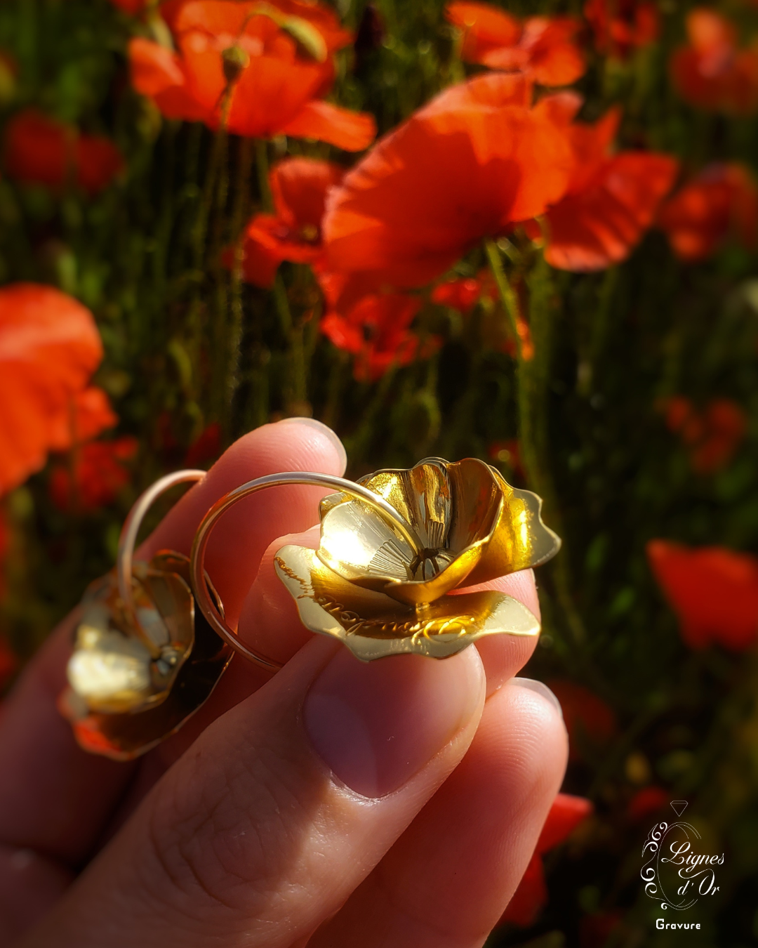 Boucles d'oreilles Coquelicots tenues entre les doigts devant un champs de coquelicots