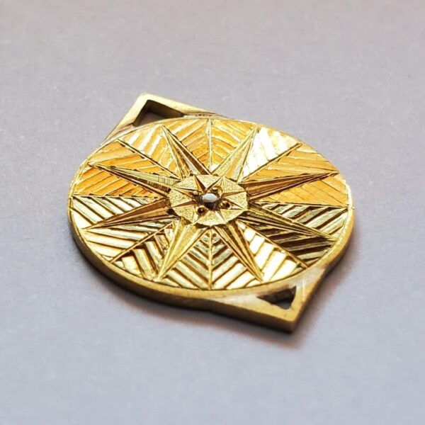 Pendentif en or gravé et serti d'un diamant, sur fond clair.