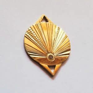 Pendentif or soleil gravé serti d'un diamant, sur fond neutre clair.