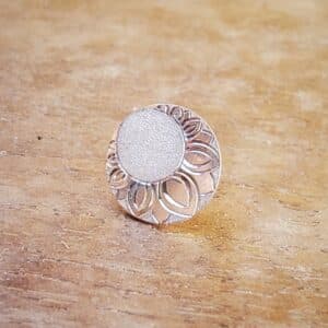 Boucle d'oreille ronde en argent et gravée d'un décor posée sur support en bois.