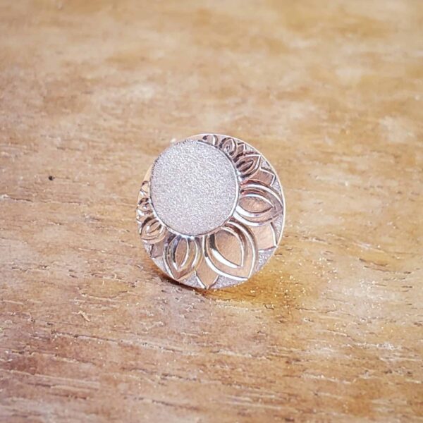 Boucle d'oreille ronde en argent et gravée d'un décor posée sur support en bois.