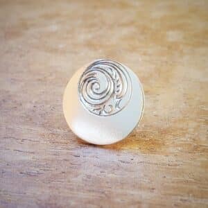 Boucle d'oreille ronde en argent et gravée d'un décor posée sur support en bois.