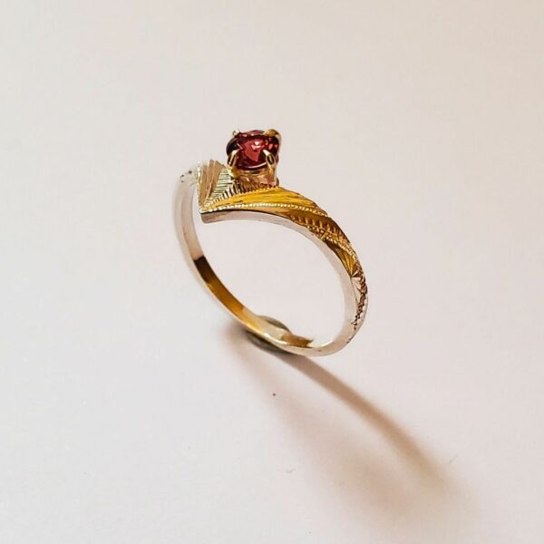 Bague sertie d'un grenat rouge, posée debout sur fond clair.