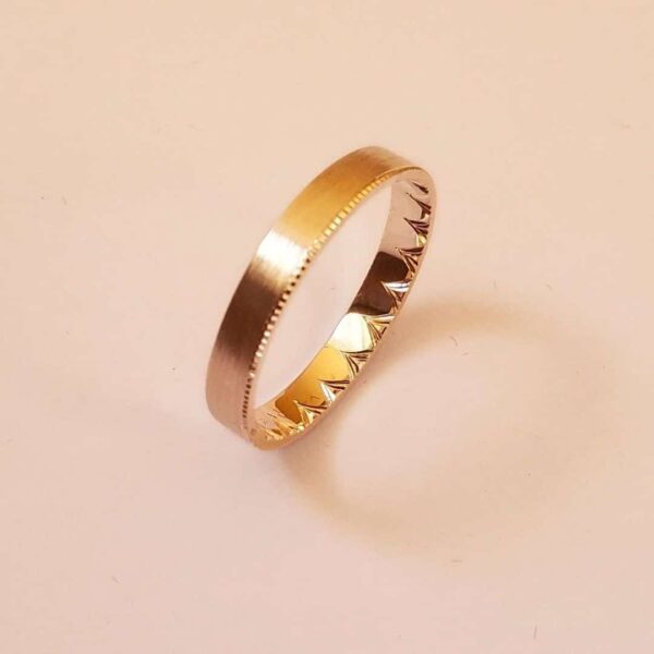 Bague en or gravée d'un motif couronne à l'intérieur. Posée debout sur fond clair.