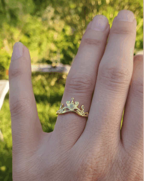 Bague diadème en or jaune portée au doigt, sur fond de verdure.