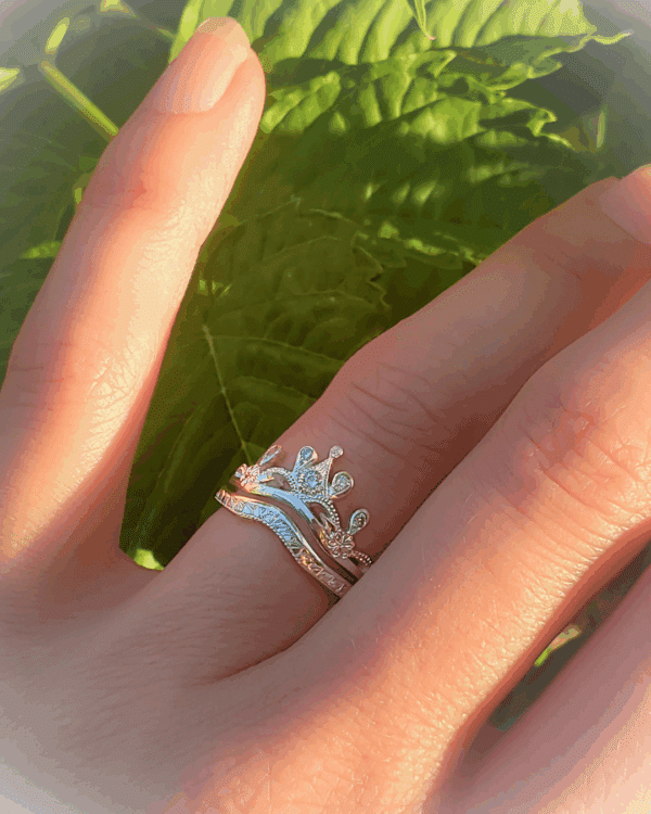 Bague diadème et son alliance complémentaire, portée au doigt, sur fond de verdure.