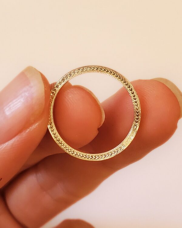 Bague Leialta tenue de profil entre les doigts pour dévoiler sa tranche gravée d'une frise végétale.