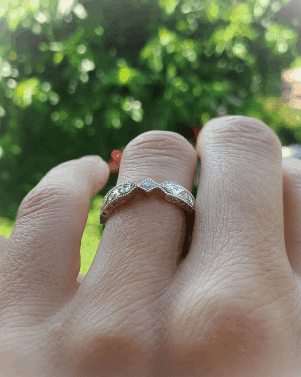 Alliance finement travaillée de volutes et diamants, portée au doigt.