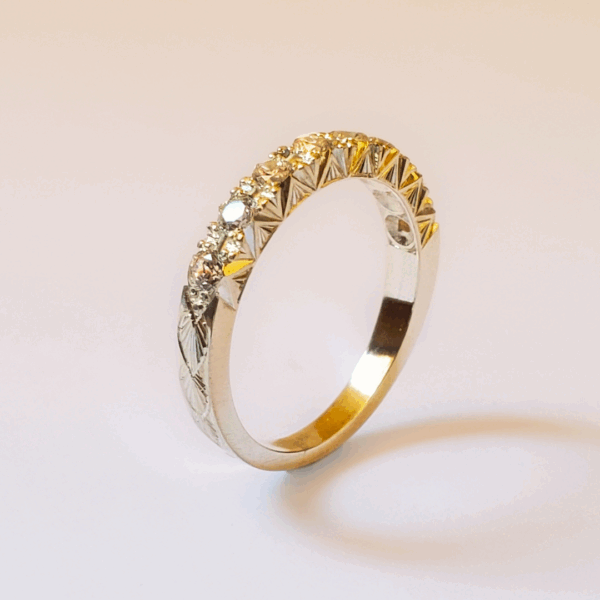 Alliance en or gravée d'un motif végétal et pavée de diamants. Debout sur fond clair.