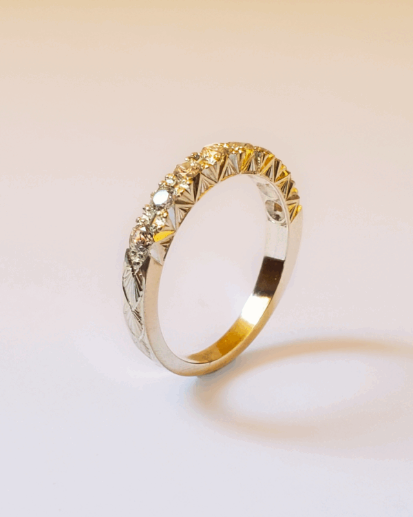 Alliance en or gravée d'un motif végétal et pavée de diamants. Debout sur fond clair.
