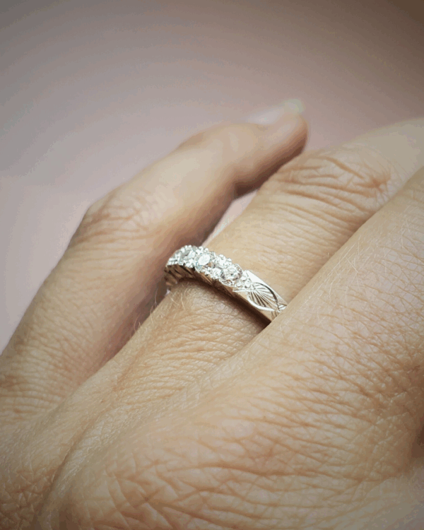 Bague de fiançailles ou alliance sertie de diamants et ornée de gravures végétales, portée au doigt.