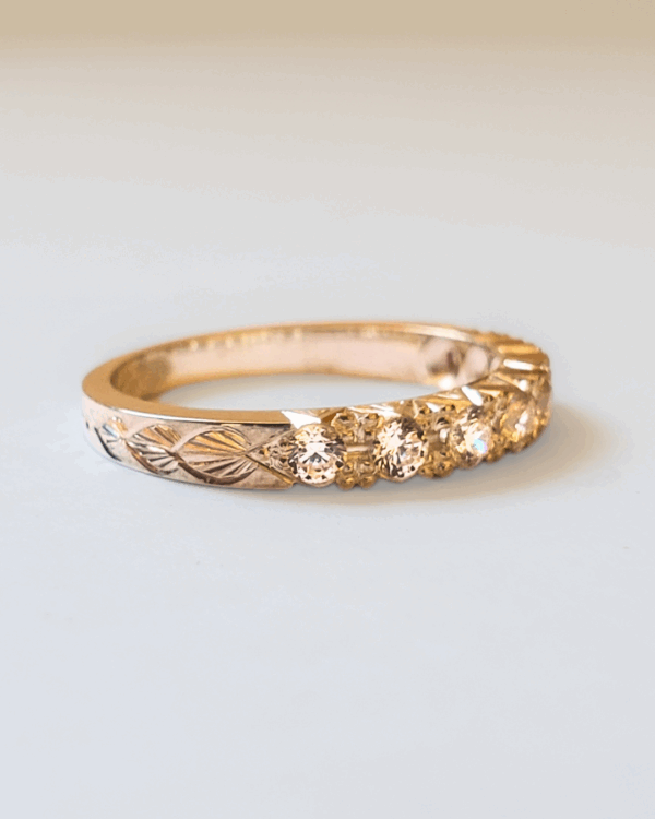 Bague de fiançailles ou alliance en or rose pavée de diamants et gravée de motif végétal. Posée sur fond clair.